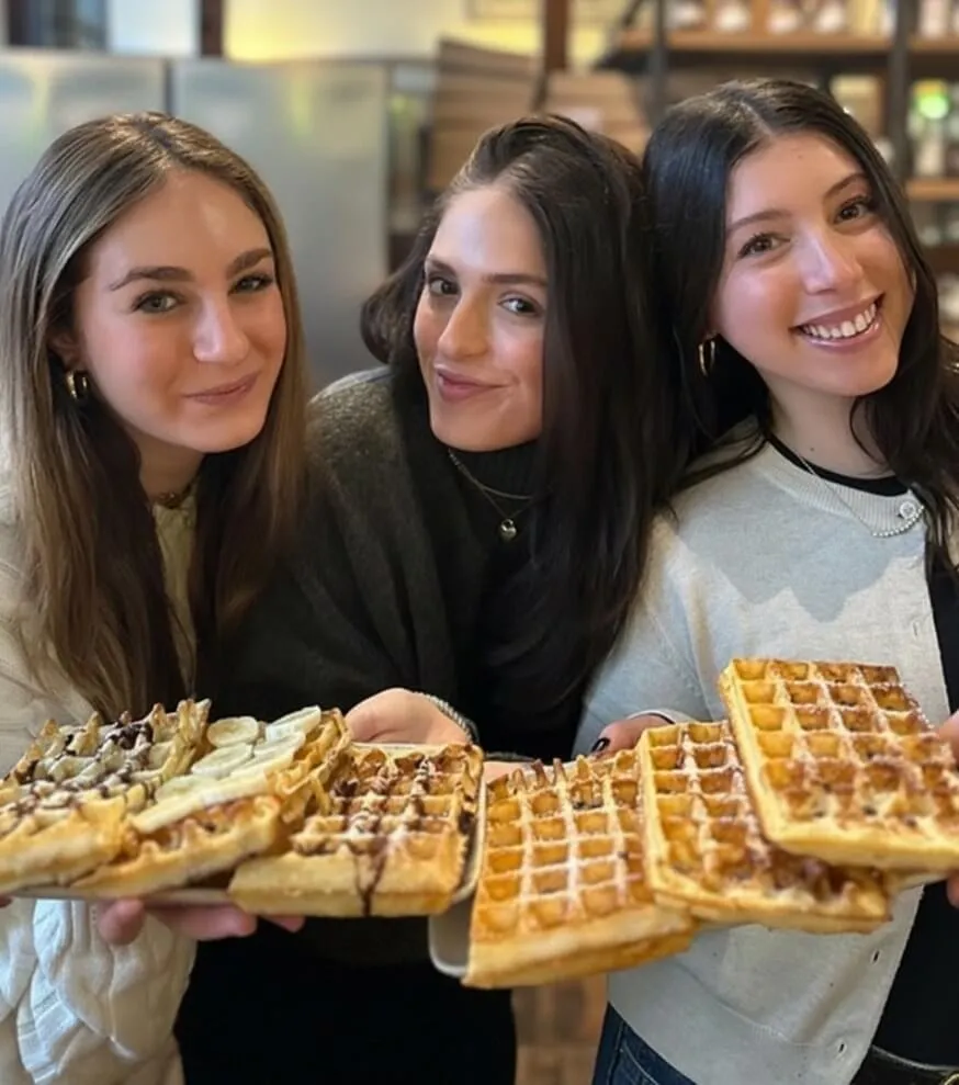 Three friends holding fresh Belgian waffles at the workshop